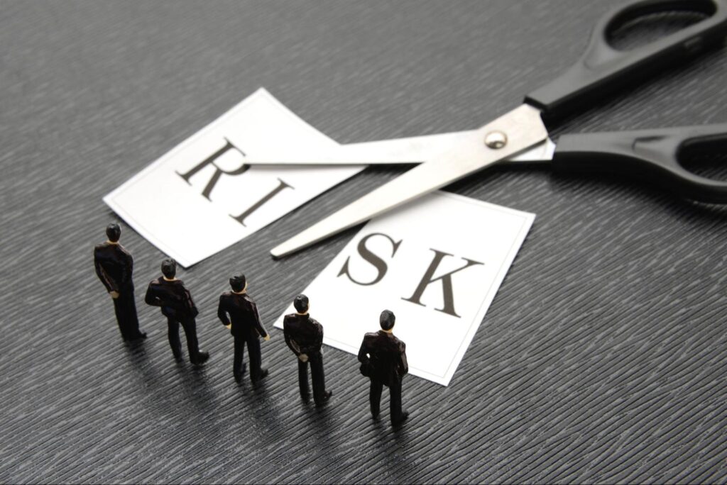 RISKと書かれた紙が半分に切られた様子とハサミ それらを見る小さな人の模型