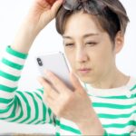 ドライアイによる実用視力低下が起き、目を細めてスマホを見ている女性